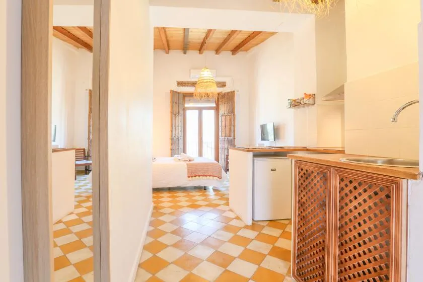 A bright bedroom opens onto a kitchenette, with patterned tile flooring and a bed.
