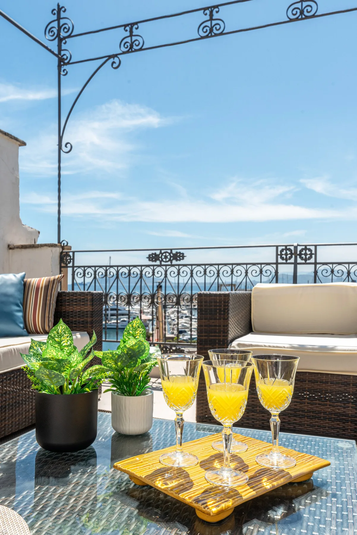 Una terraza en la azotea tiene asientos al aire libre, plantas en macetas y bebidas sobre una mesa de vidrio.