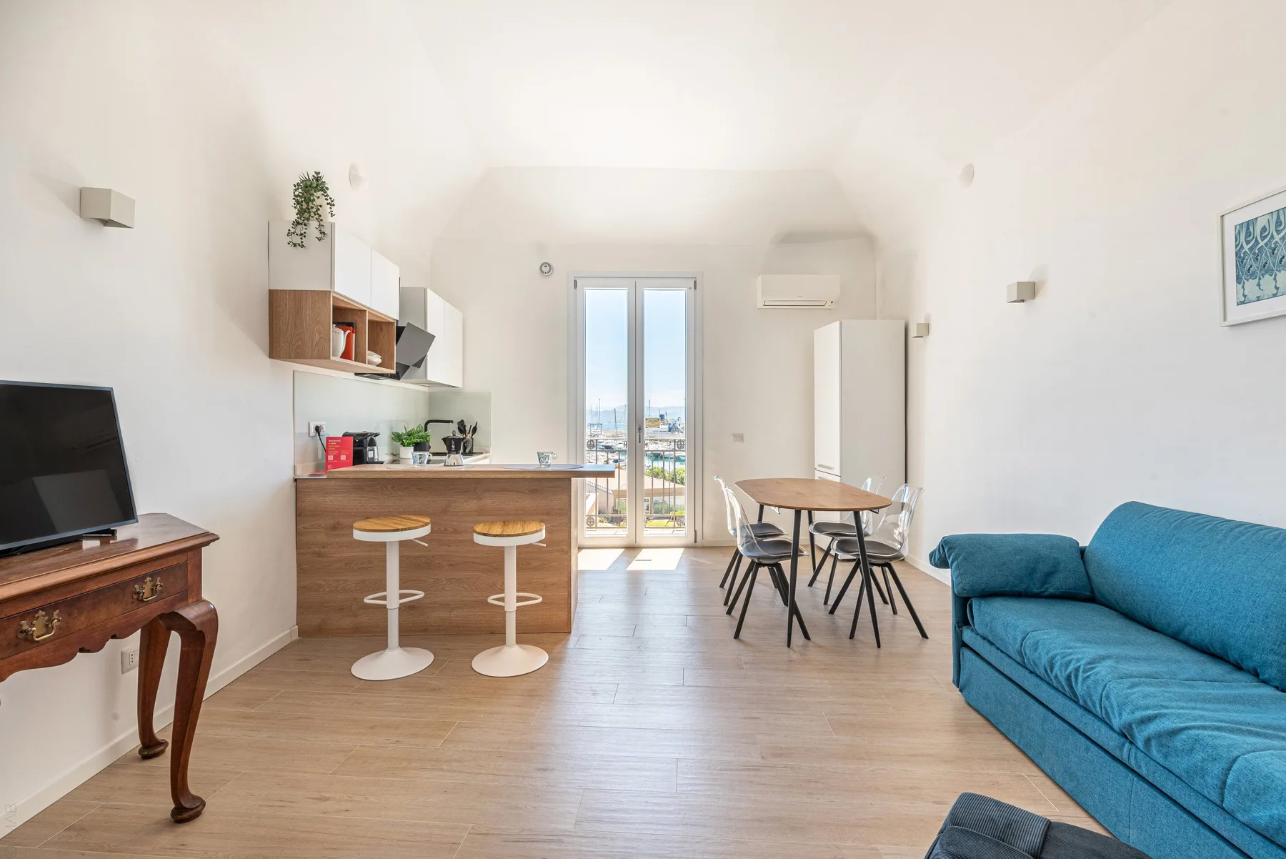 Sala-comedor diáfana y luminosa con barra de cocina y asientos azules.