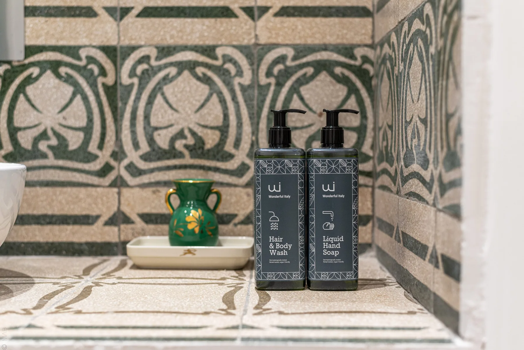 Un lavabo de baño con azulejos estampados y dos dispensadores de artículos de aseo.