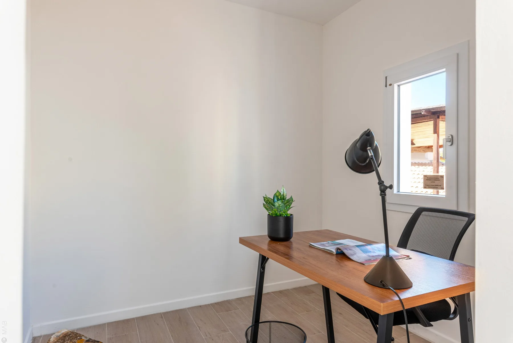 Un espacio de trabajo luminoso con escritorio de madera, lámpara y ventana.