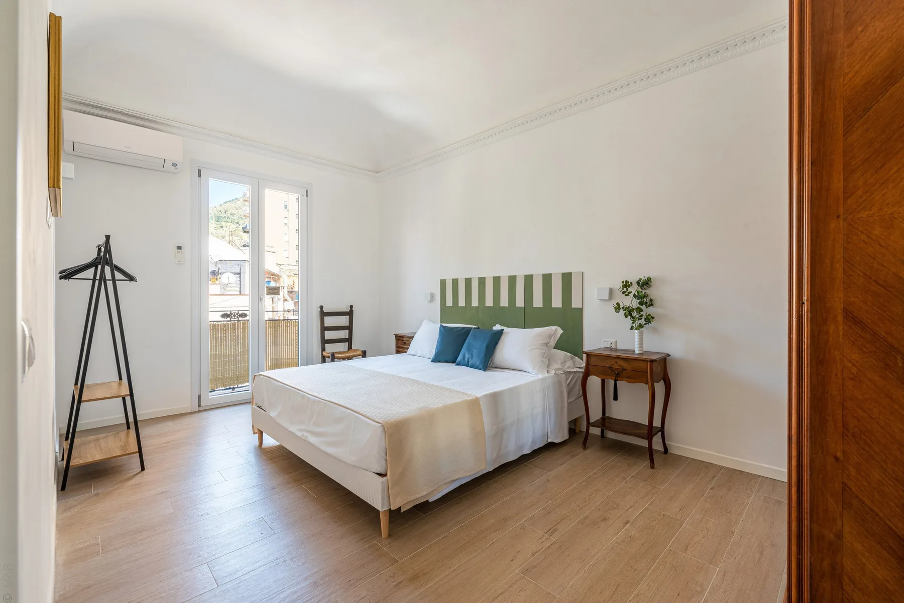 Un dormitorio luminoso con una cama, cabecero verde y puertas al balcón.