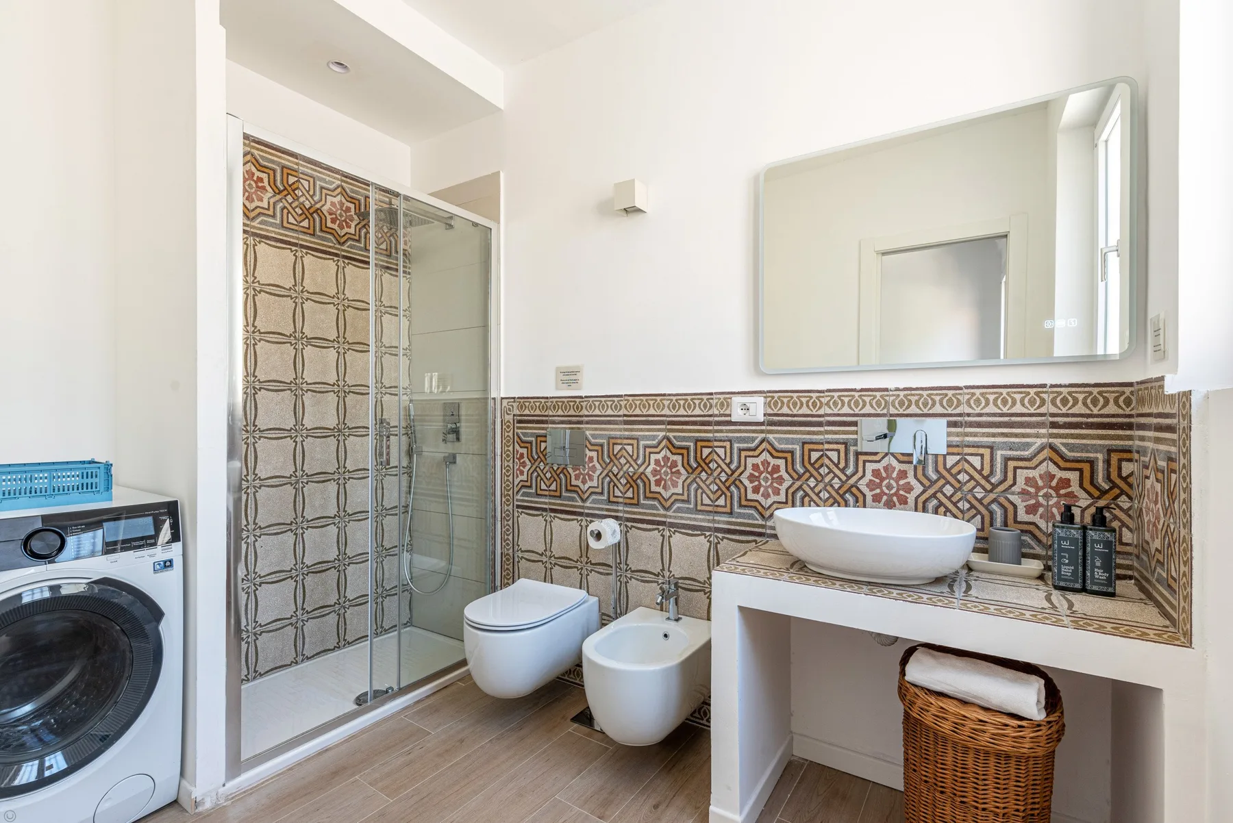 Un baño luminoso con ducha de vidrio, azulejos decorados y lavabo.