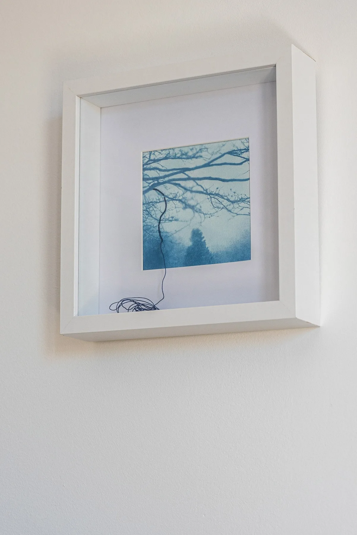 A framed blue-toned print hangs on a plain light-colored wall.
