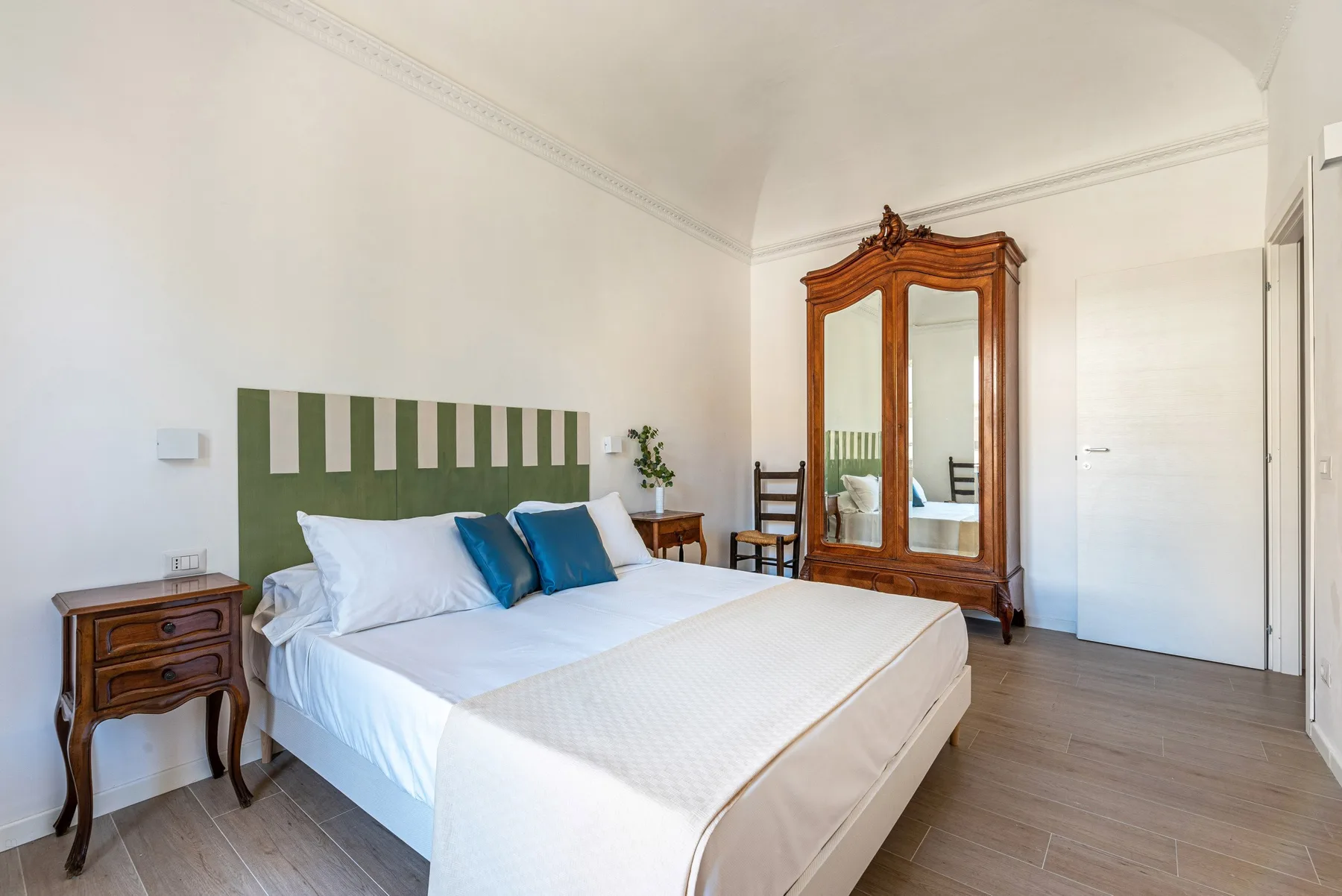 Un dormitorio luminoso con una cama doble y un armario de madera con espejo.