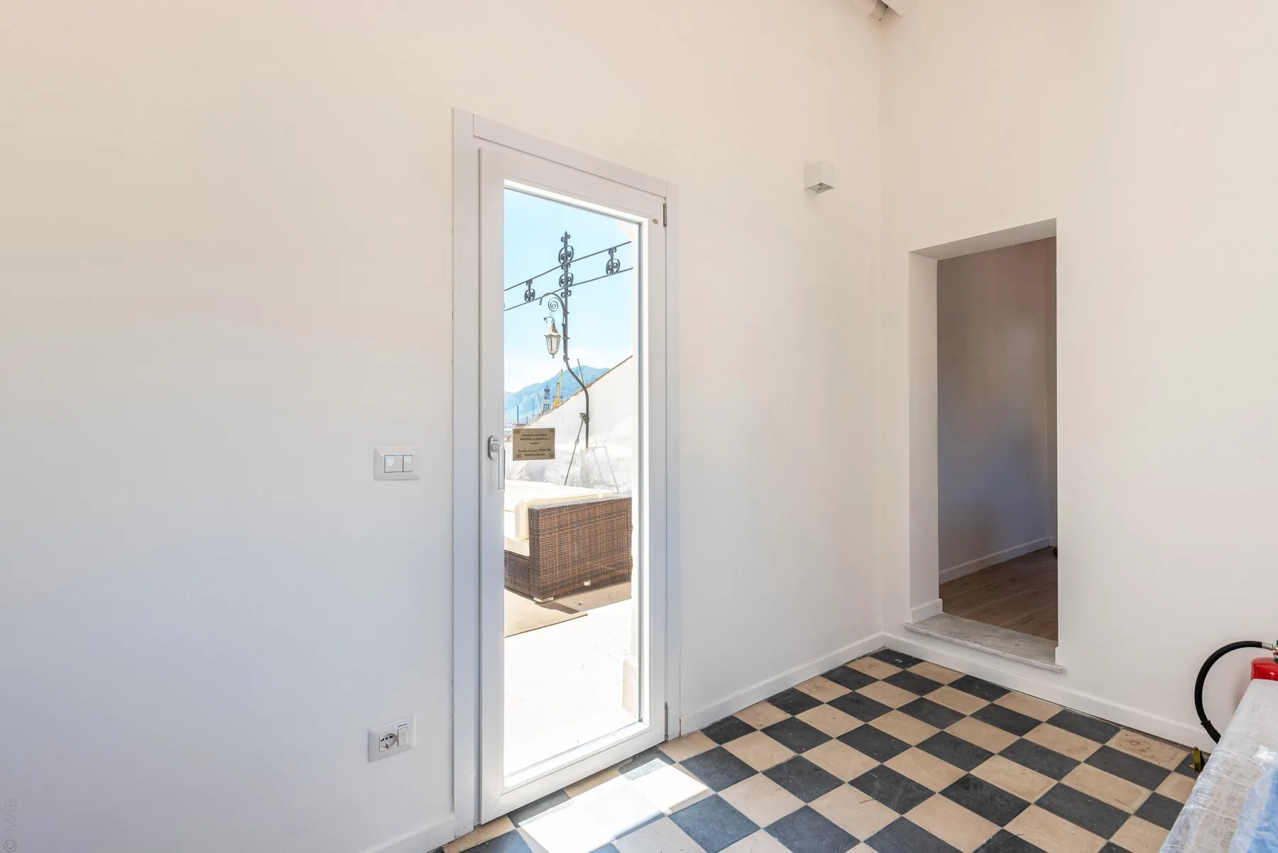 Una entrada luminosa tiene una puerta de vidrio que da a una zona exterior soleada.