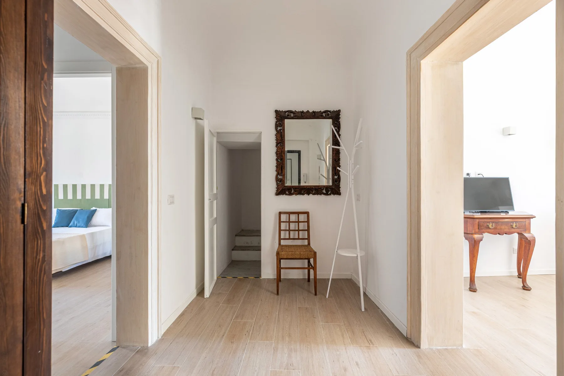 Un pasillo luminoso con una silla de madera y un espejo entre habitaciones contiguas.