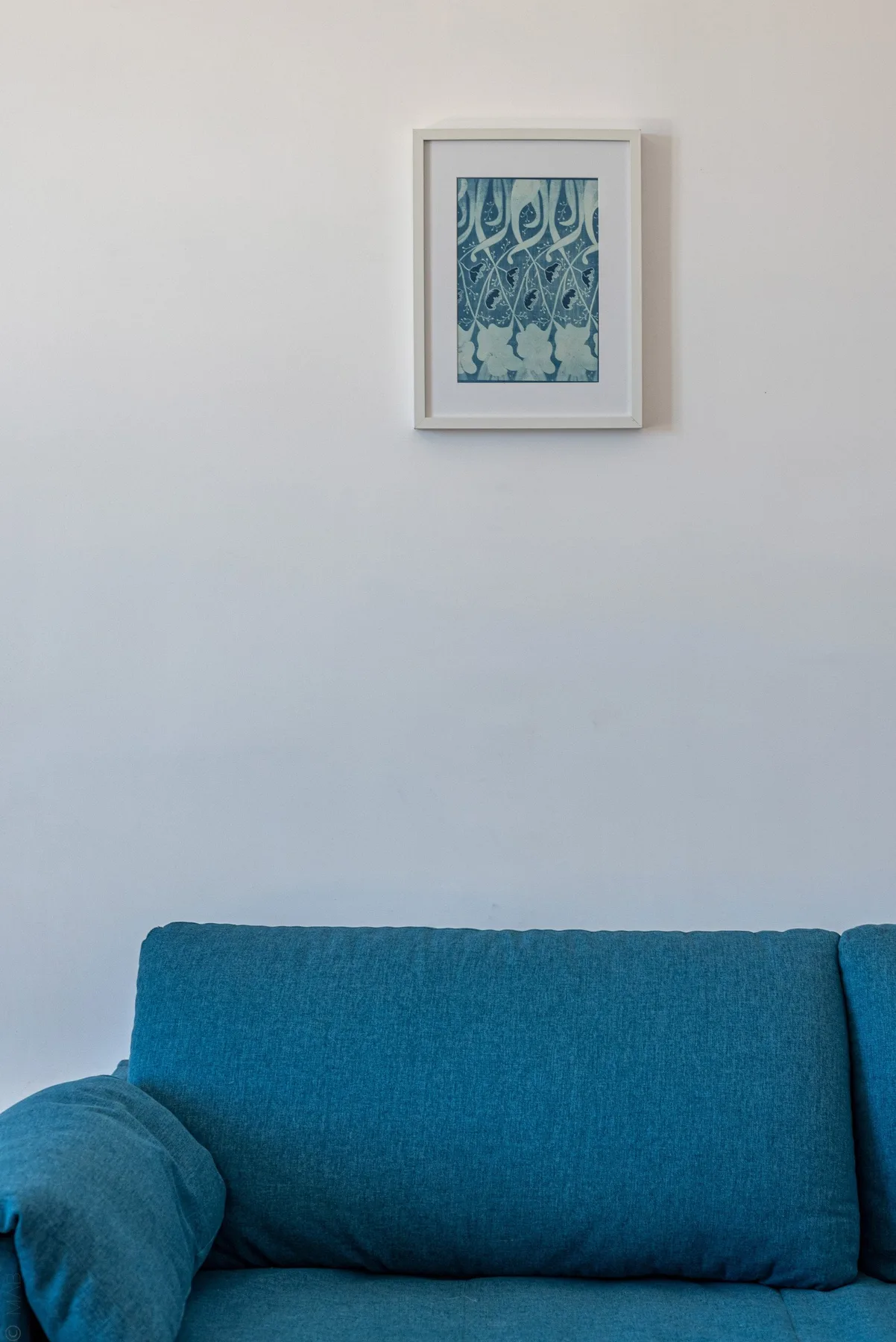 A blue sofa sits against a plain wall beneath a framed artwork.