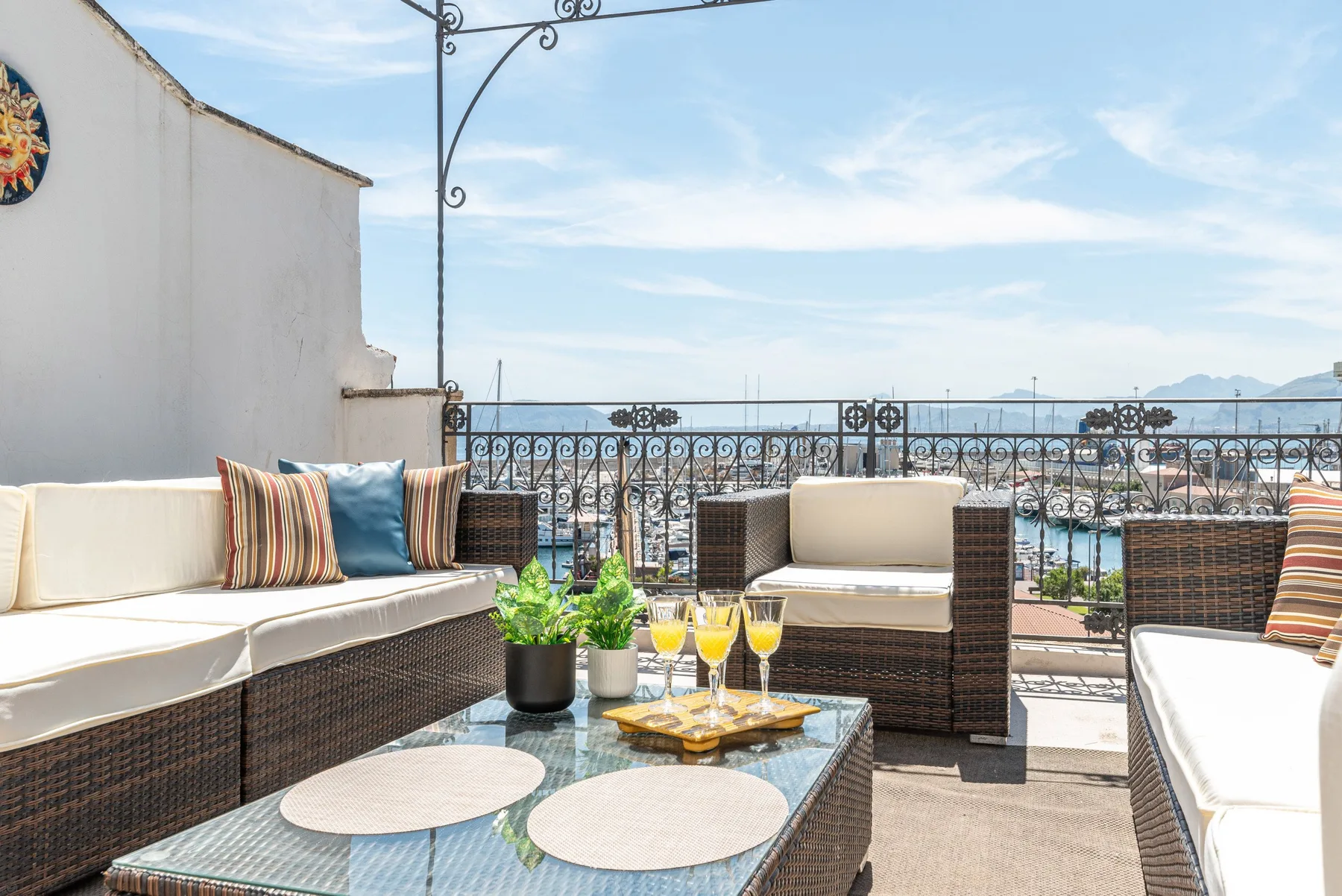 Una terraza al aire libre tiene asientos acolchados, una mesa de vidrio y vistas de la ciudad.