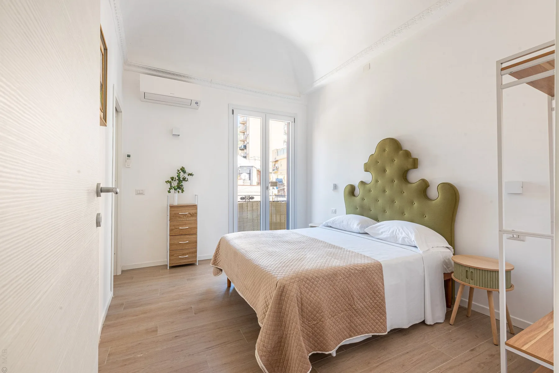 Un dormitorio luminoso con una cama, una cómoda pequeña y puertas de vidrio que dan a un balcón.