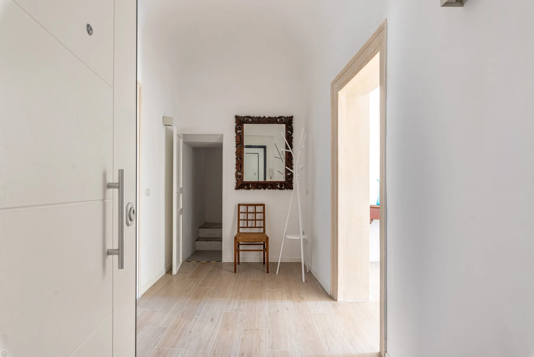 Un pasillo luminoso con un espejo, una silla y varias puertas.