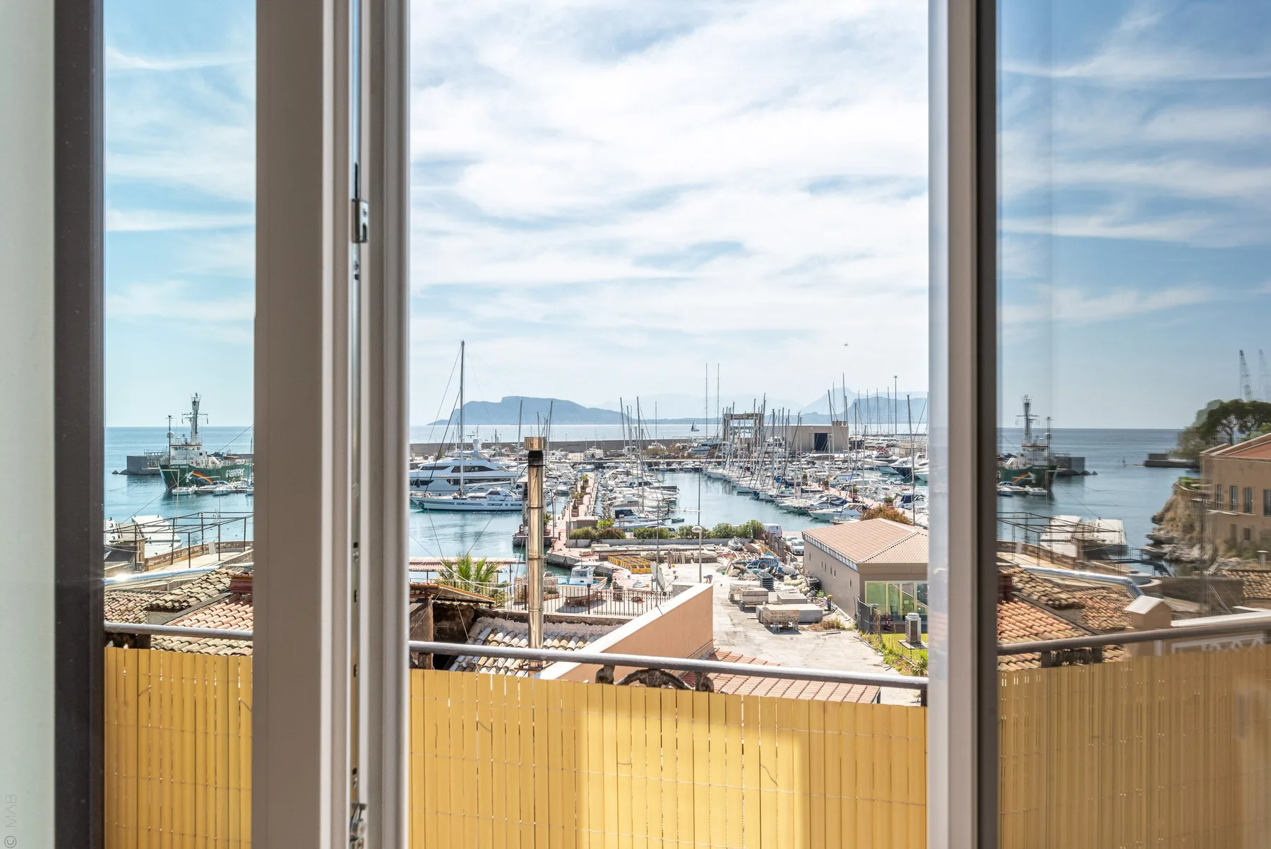 Se ve un puerto deportivo a través de ventanas altas, sobre una barandilla amarilla.