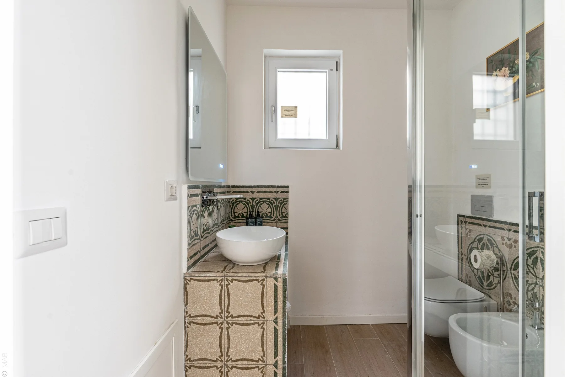 Un baño luminoso con lavabo sobre encimera, mueble estampado y ducha de cristal.