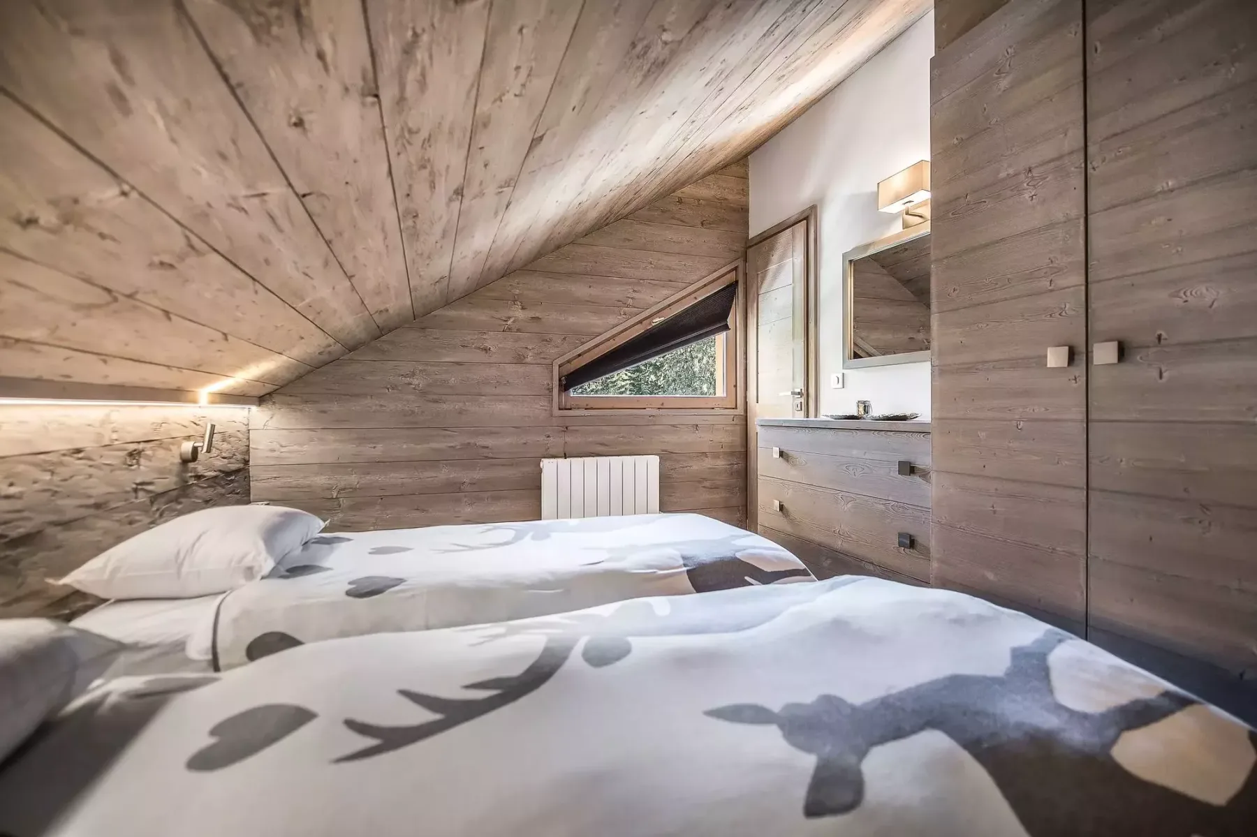 A bedroom with two beds, wood-paneled walls, and a sloped ceiling.