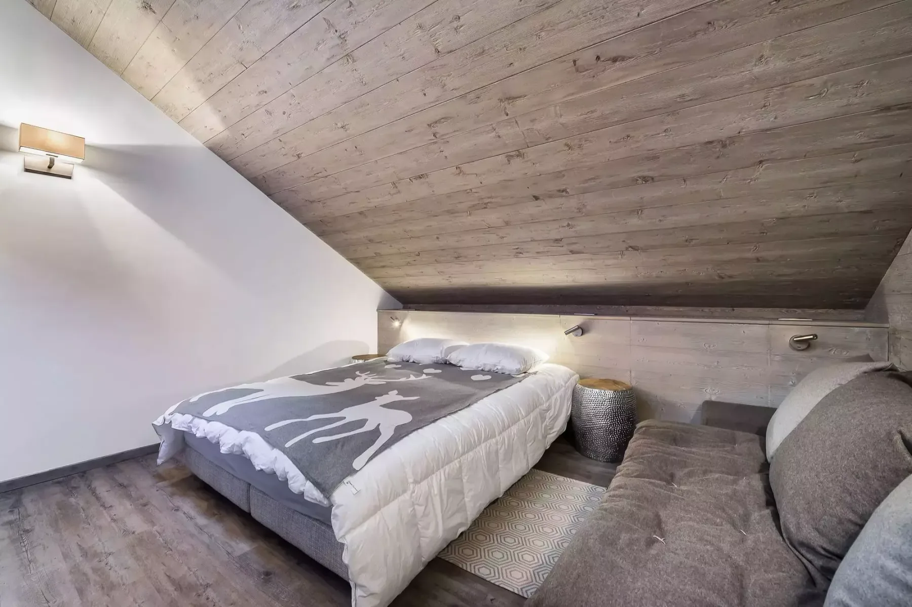 Dormitorio con una cama y asientos bajo un techo inclinado.
