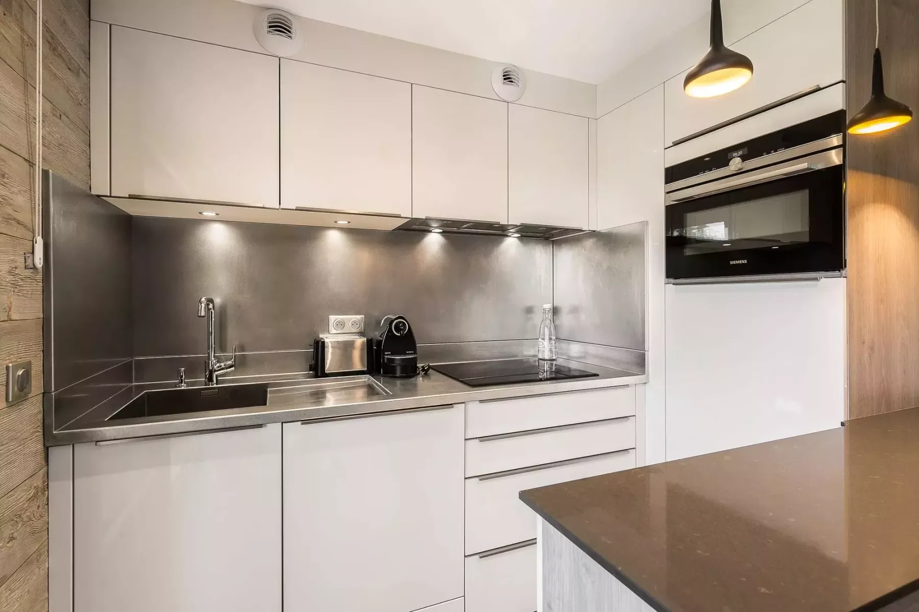 A modern kitchen with white cabinets and a stainless steel backsplash.