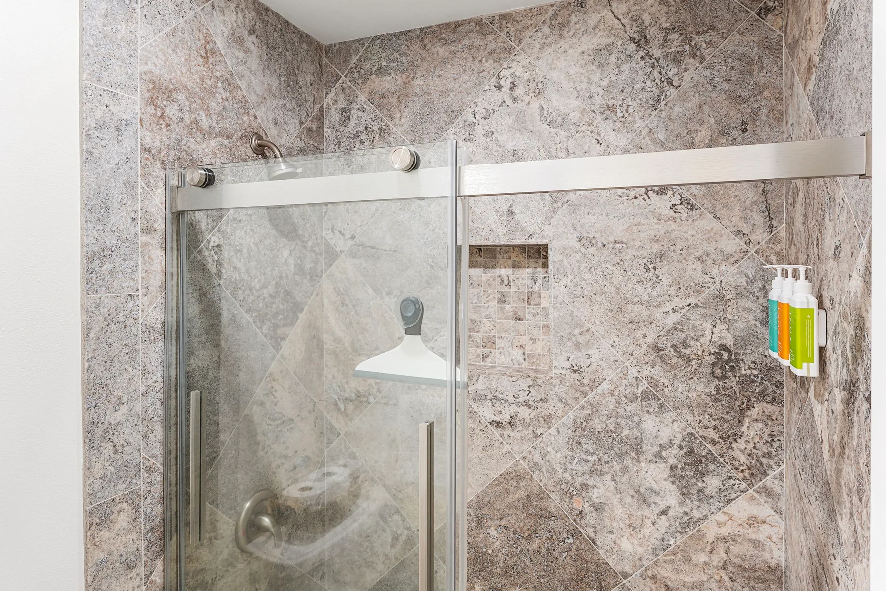Una ducha con paredes de azulejos, panel de vidrio y artículos de baño en la pared.