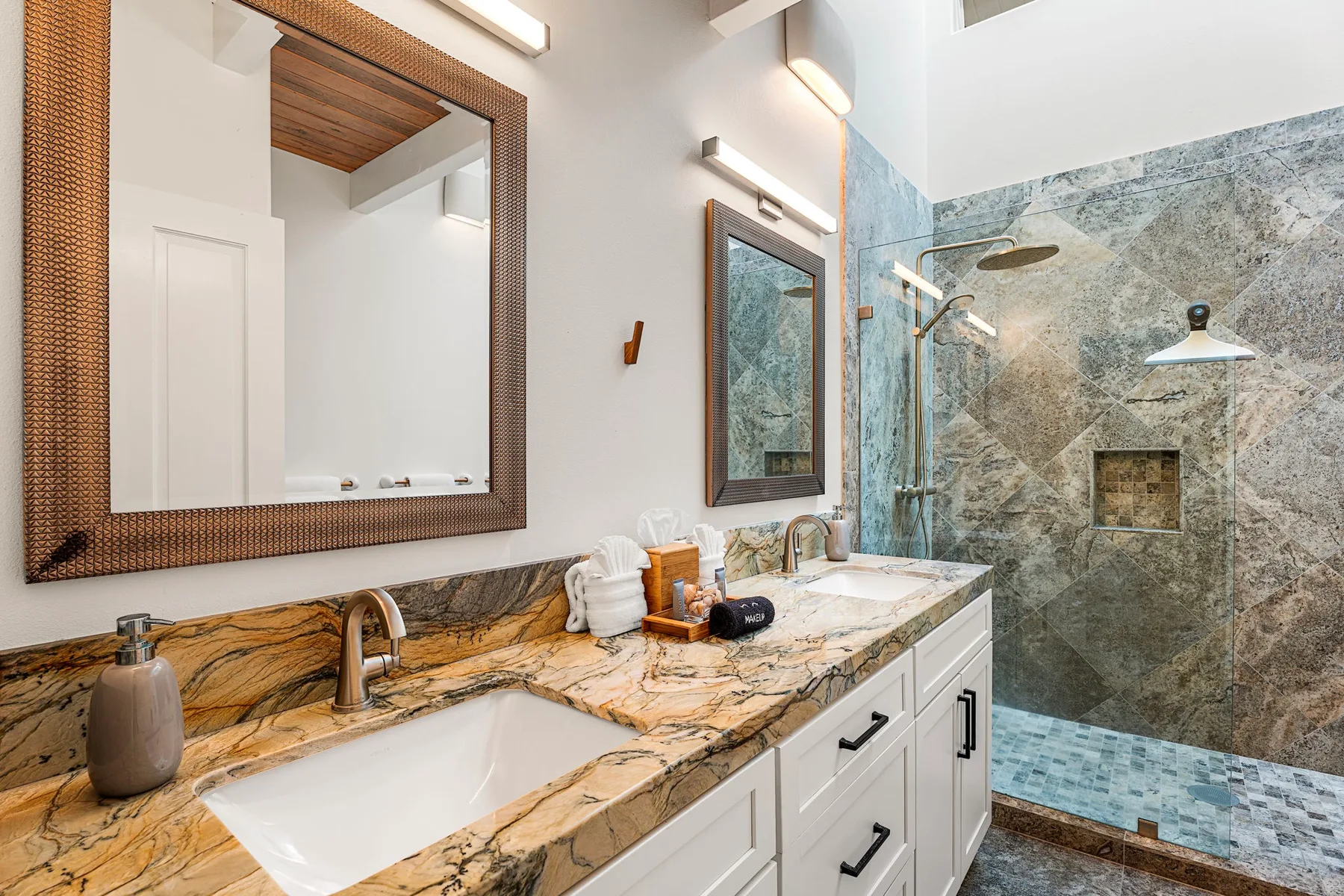Un tocador de baño con encimera de piedra está junto a una ducha revestida de azulejos.