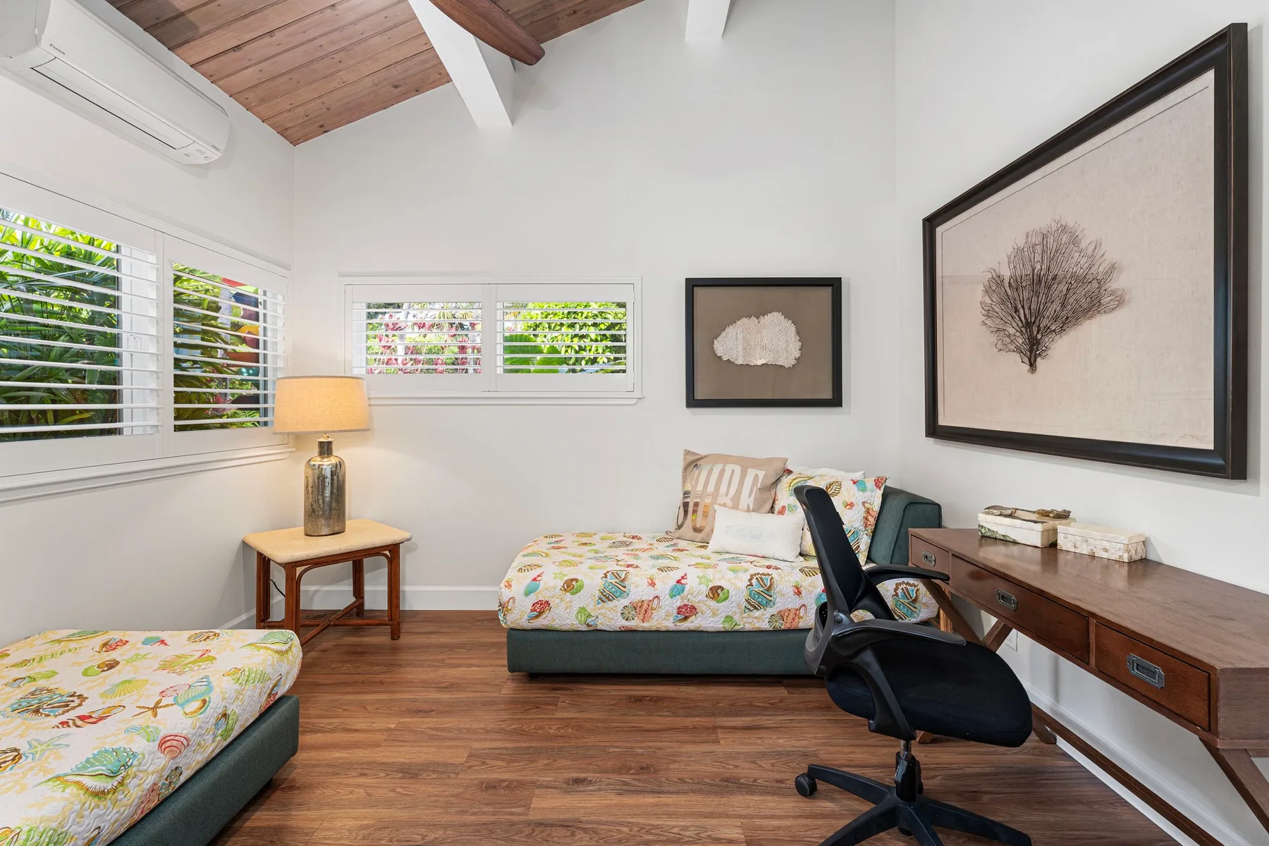 Un dormitorio luminoso con camas, una silla de escritorio y láminas botánicas enmarcadas.