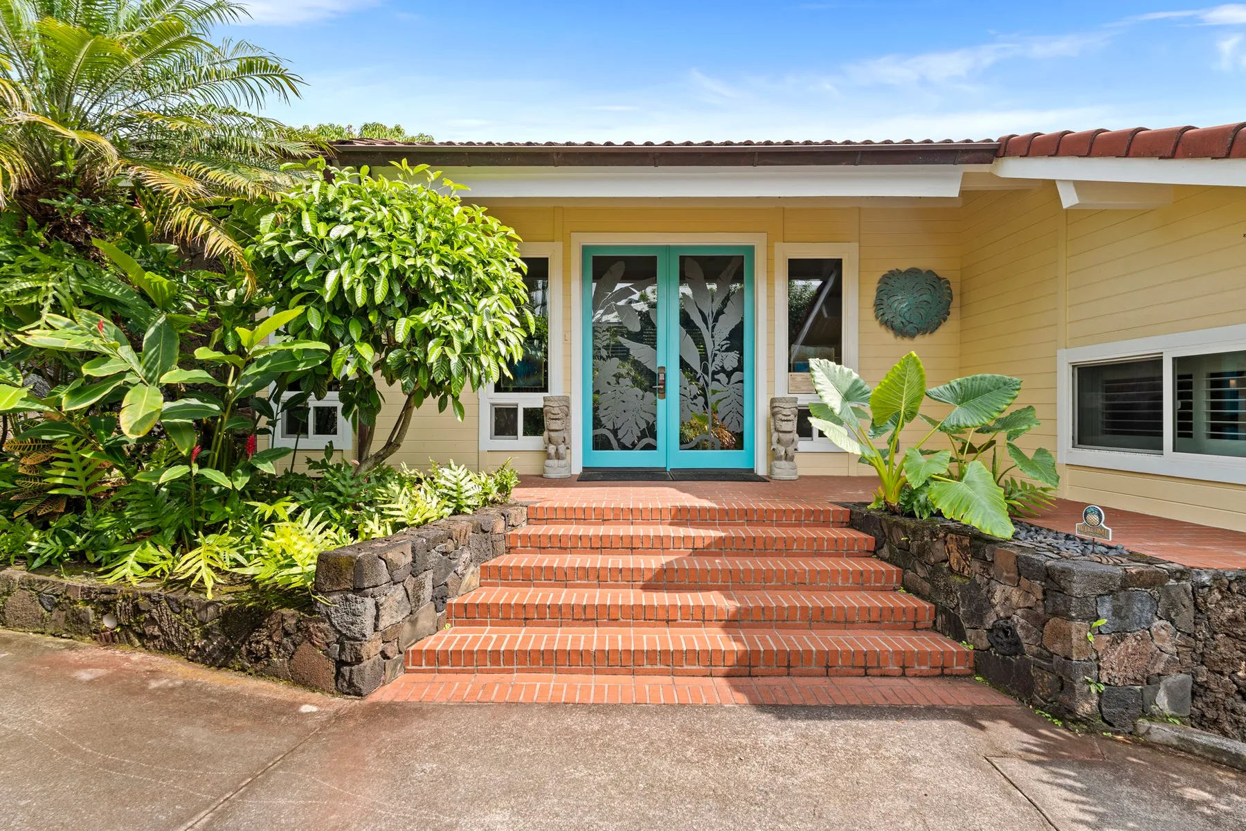 Entrada de una casa con escalones de terracota y exuberante vegetación tropical.