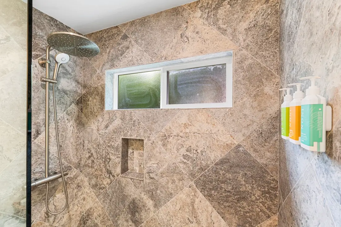 Una zona de ducha con paredes de efecto piedra y una pequeña ventana horizontal.