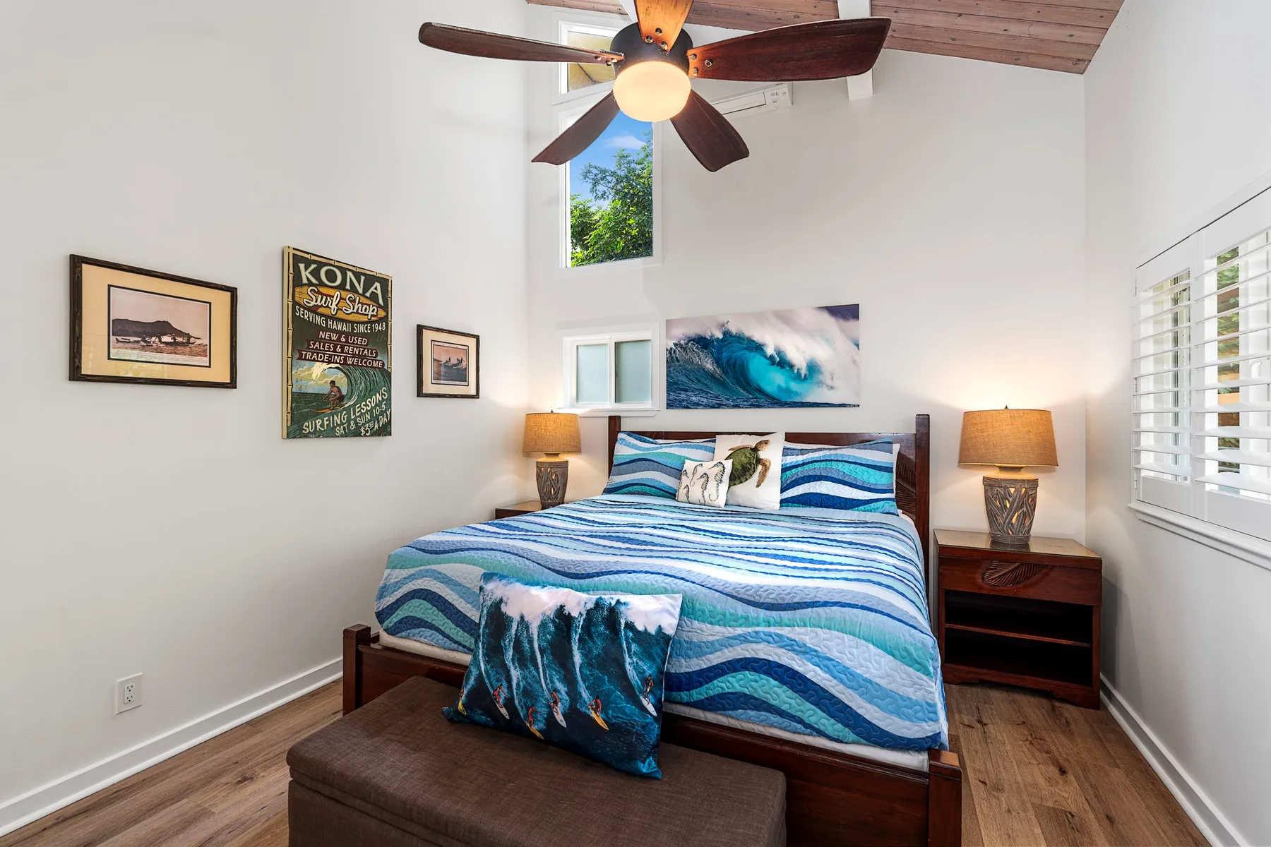 Un dormitorio con una cama tendida, ropa de cama azul con olas y cuadros.