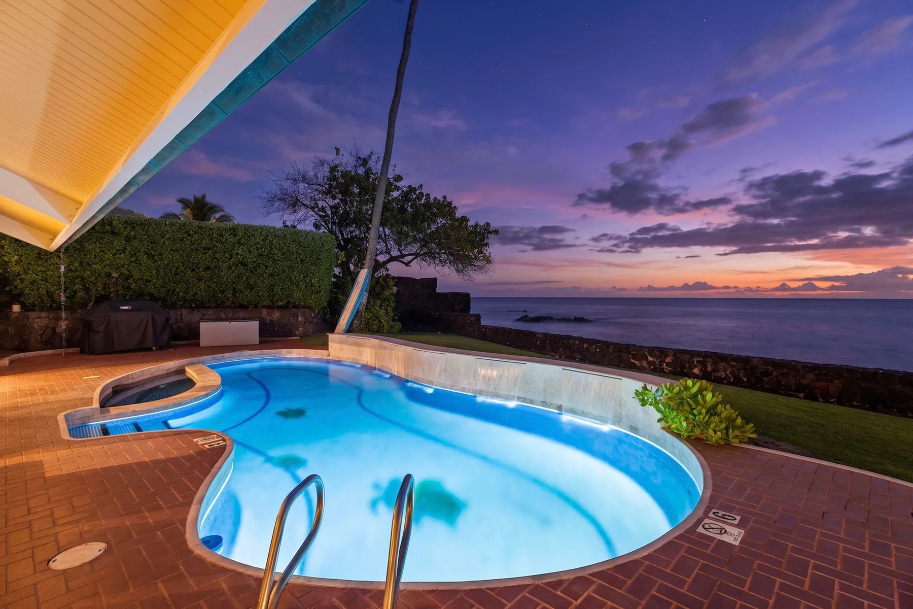 Una piscina al aire libre mira hacia el océano bajo un cielo colorido al atardecer.