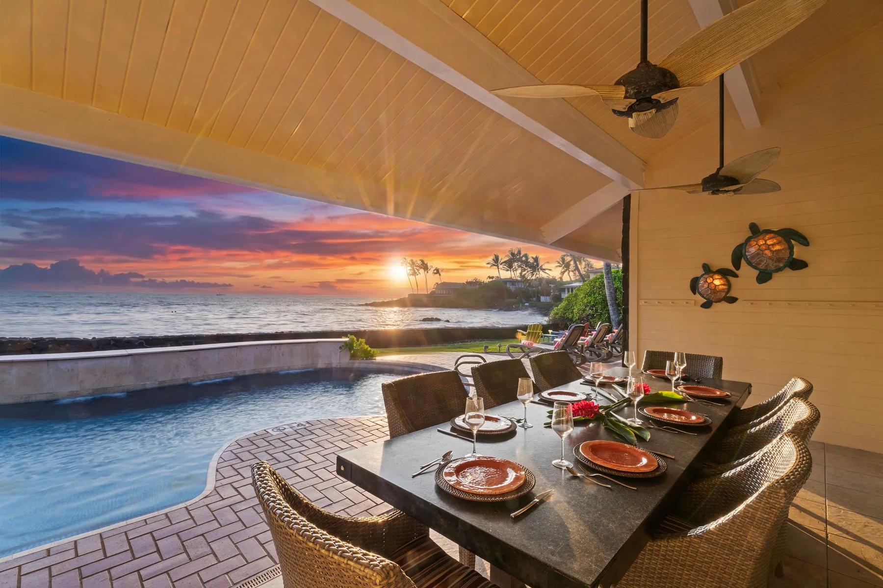 Un comedor exterior cubierto da a una piscina y al atardecer sobre el mar.