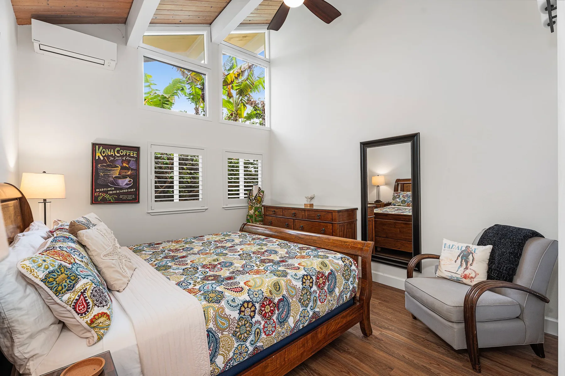 Un dormitorio luminoso con una colcha estampada, ventanas altas y techo de madera.