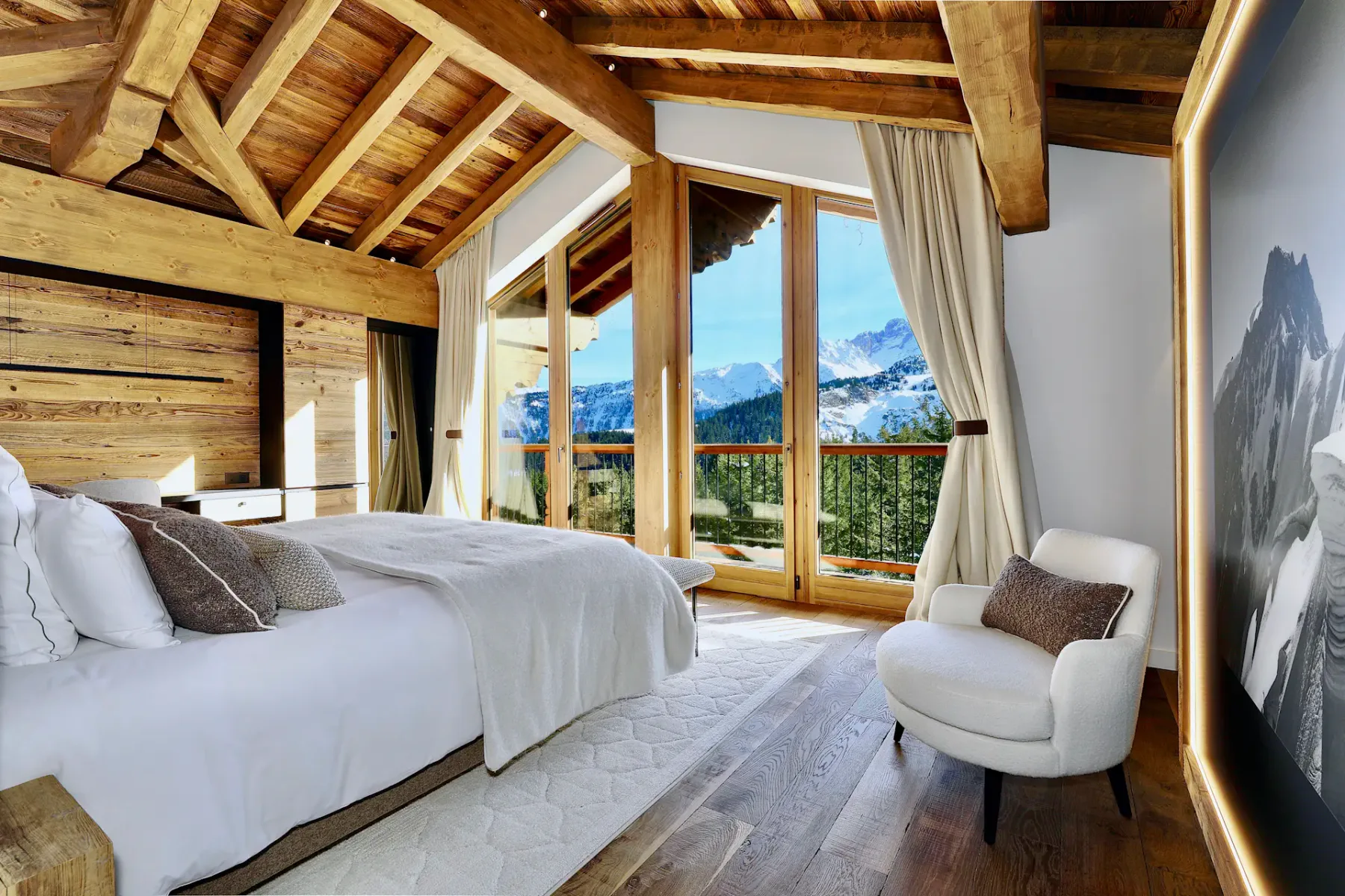 Un dormitorio con vigas de madera a la vista, una cama y ventanas con vistas a un paisaje montañoso.