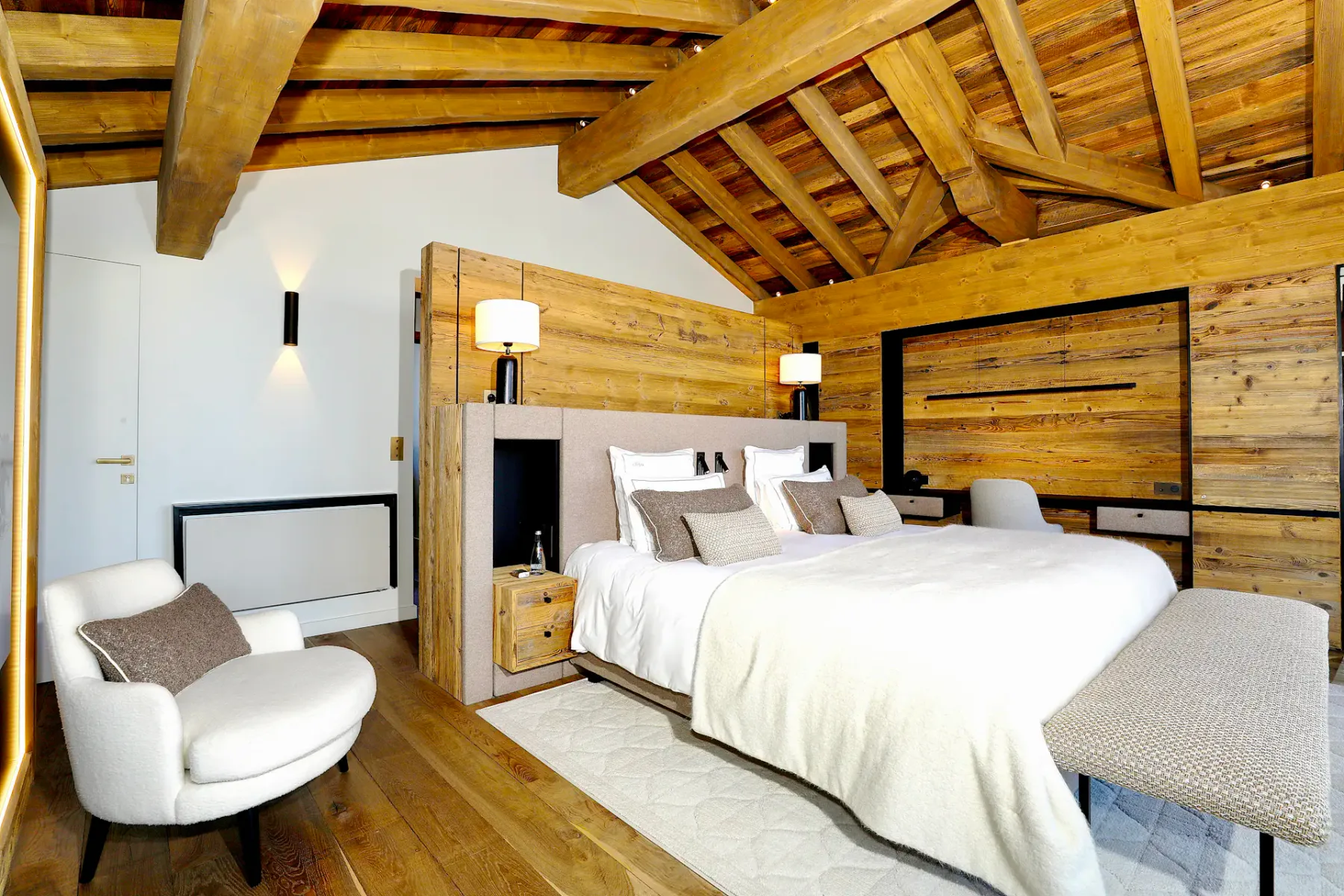 Acogedor dormitorio con paredes y techo de madera, una cama grande, iluminación suave y un mullido sillón.