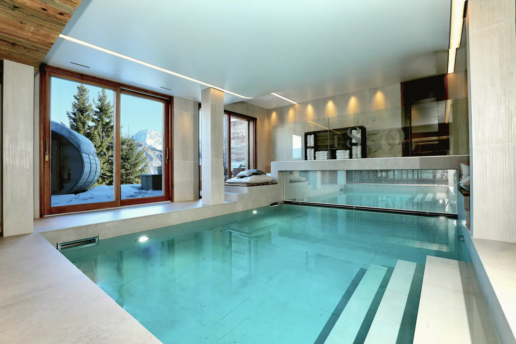 Piscina interior de agua cristalina, rodeada de decoración moderna. Las grandes ventanas ofrecen vistas a los árboles nevados y las montañas del exterior.