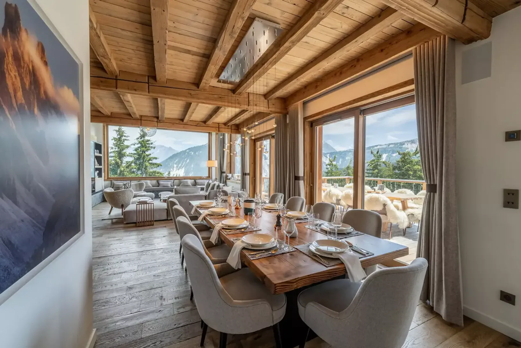 Spacious dining room with a wooden table set for eight, large windows offering mountain views, and cozy seating in a rustic, elegant interior.