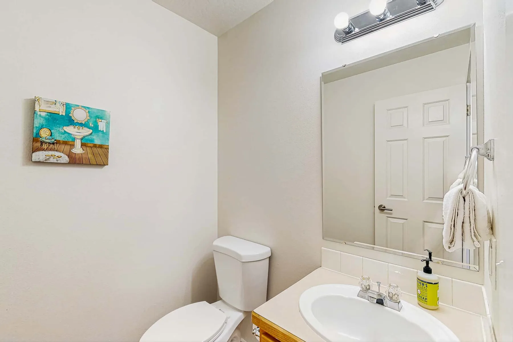 A bathroom with a sink, toilet, and large wall mirror.