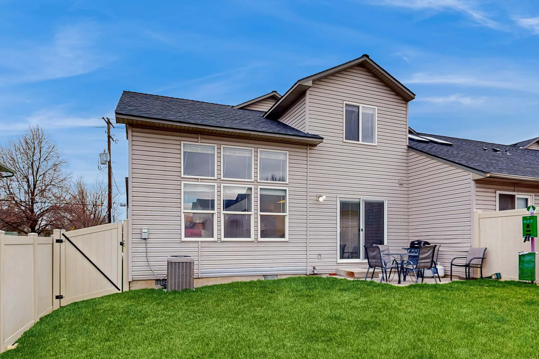 A two-story house stands behind a green lawn, with a patio seating area beside it.