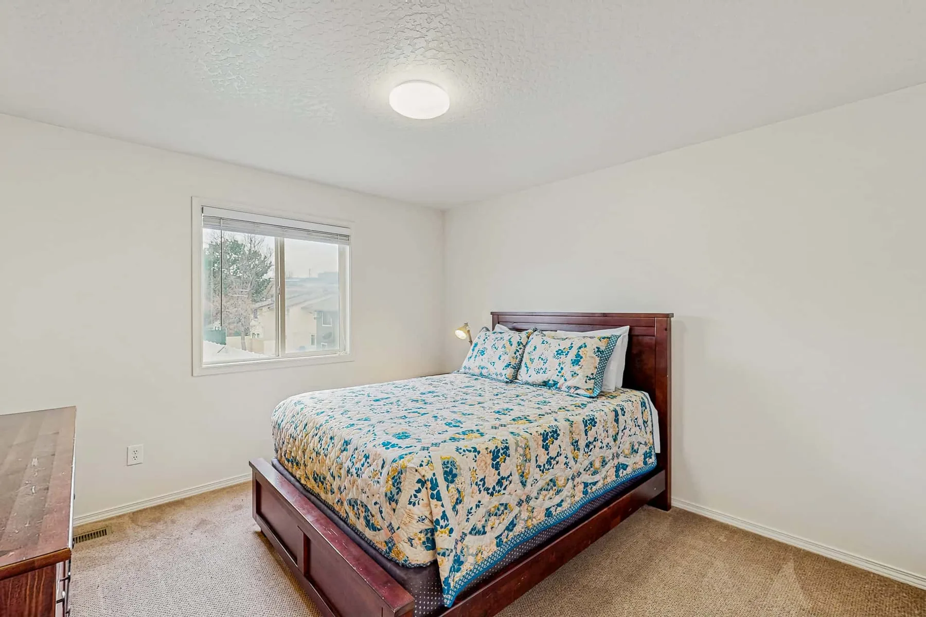 A bedroom with a bed covered in a blue-and-yellow floral quilt beside a window.