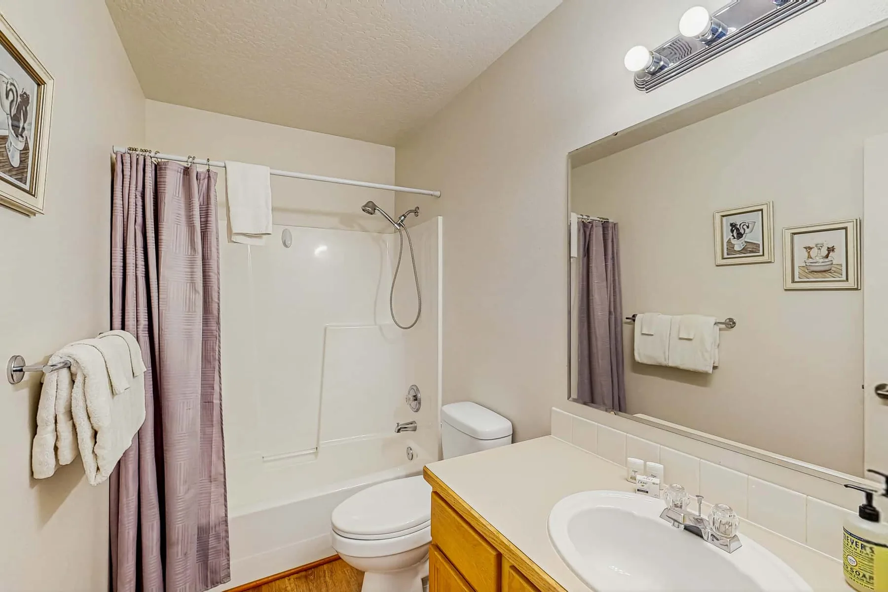A bathroom with a bathtub, toilet, and vanity beneath a large mirror.