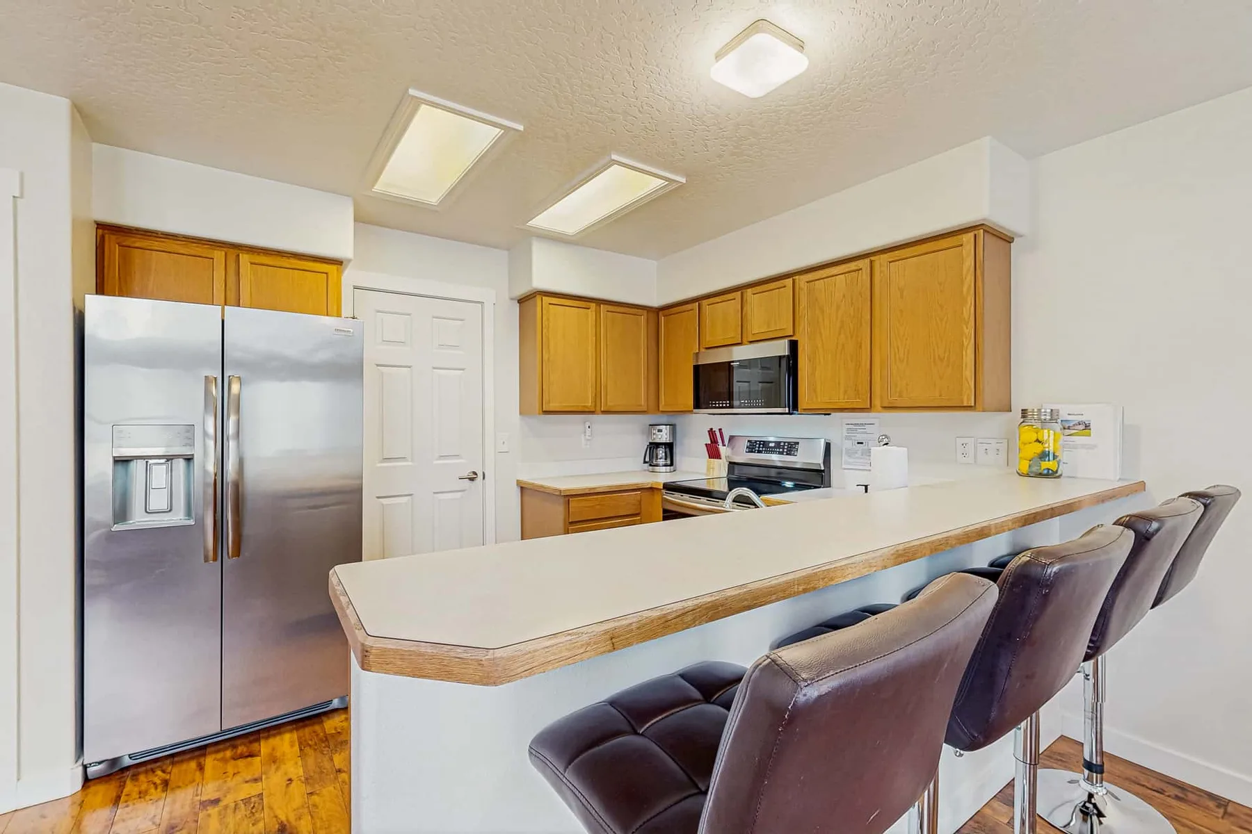 A bright kitchen with wood cabinets, stainless steel appliances, and a long counter with seating.