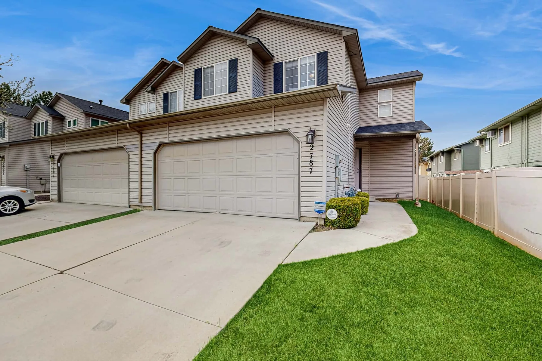 A multi-unit residential building faces a broad driveway, with a small lawn beside it.