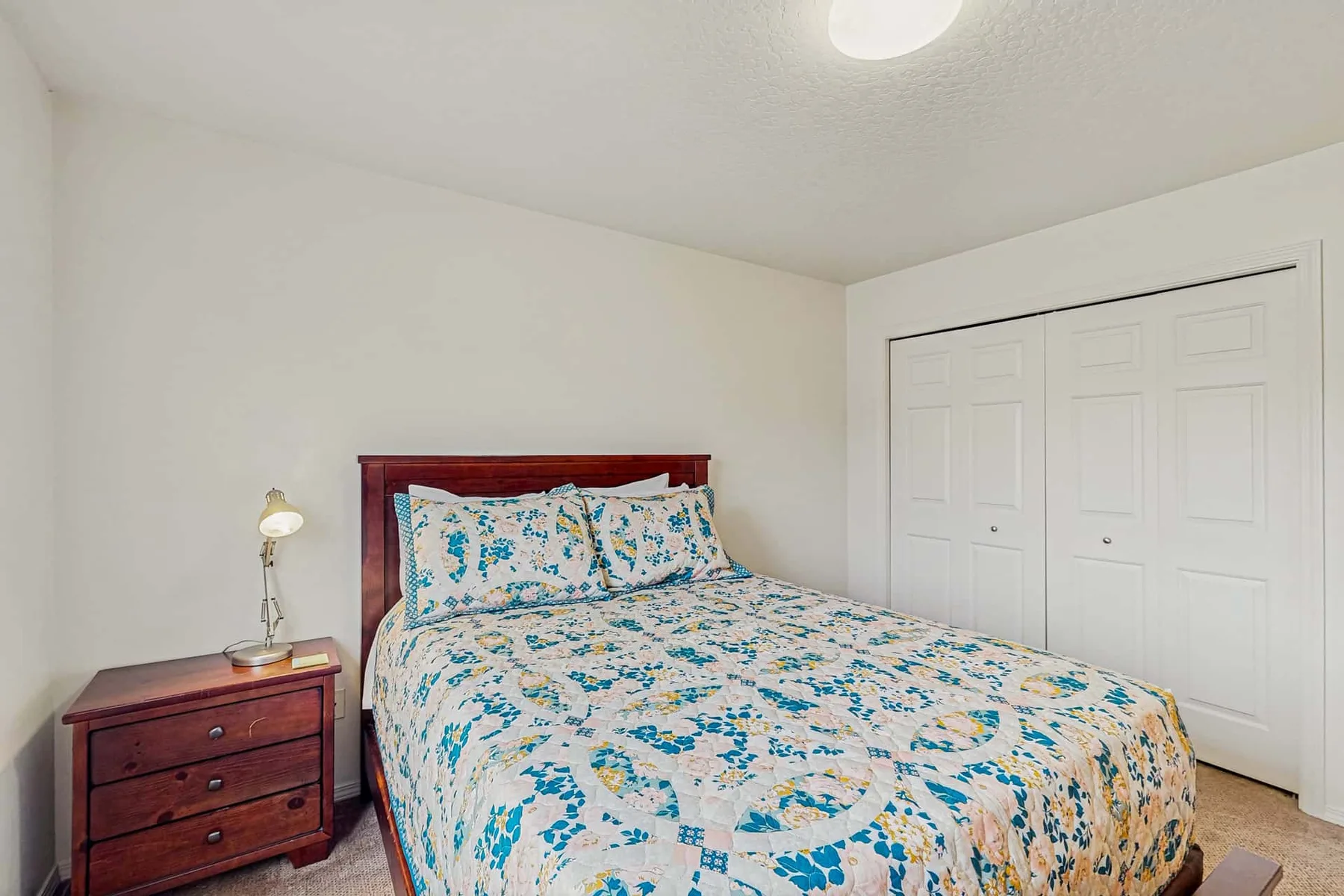 A bedroom with a bed covered in a blue-and-white patterned quilt.