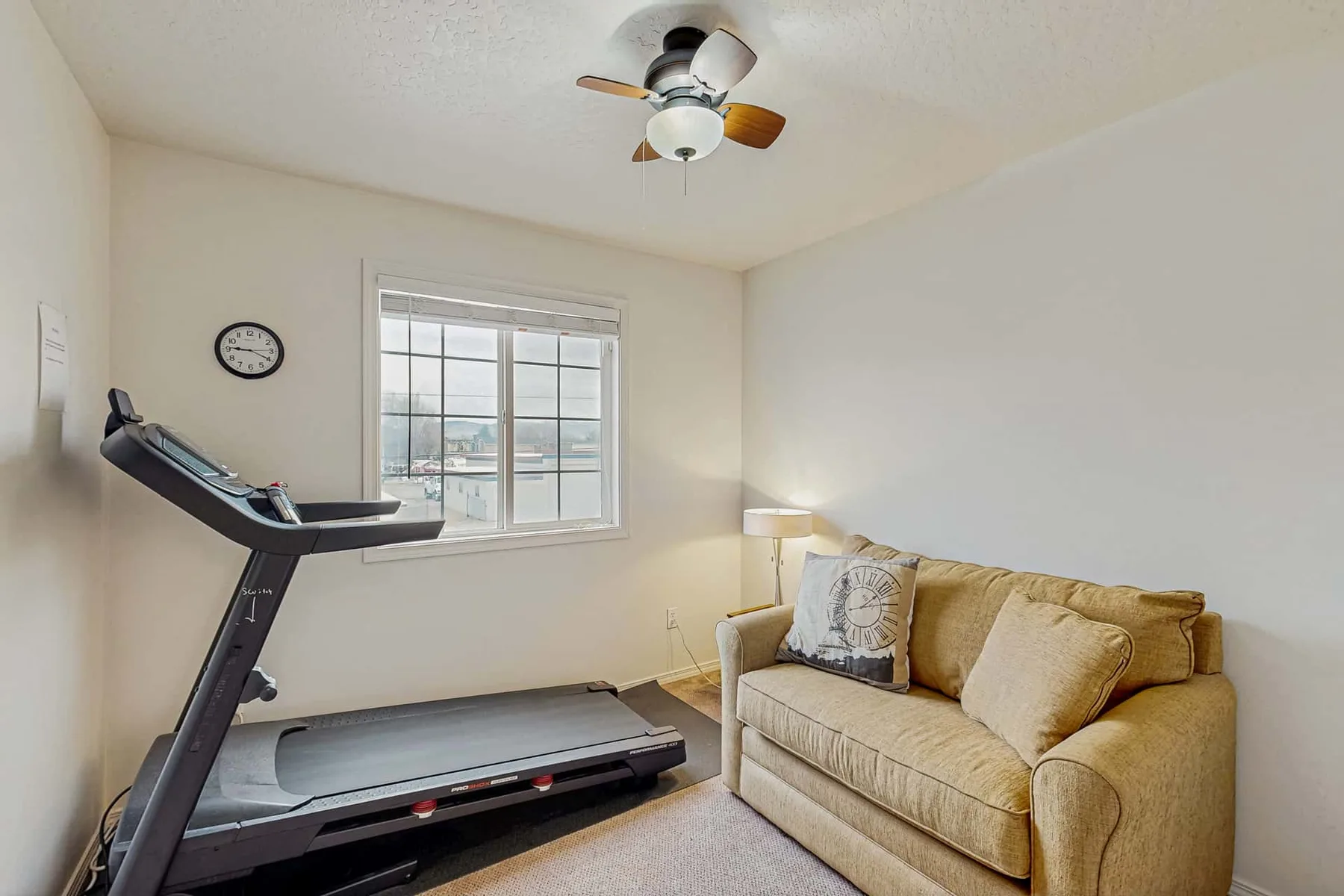 A living room with a treadmill beside a couch and window.