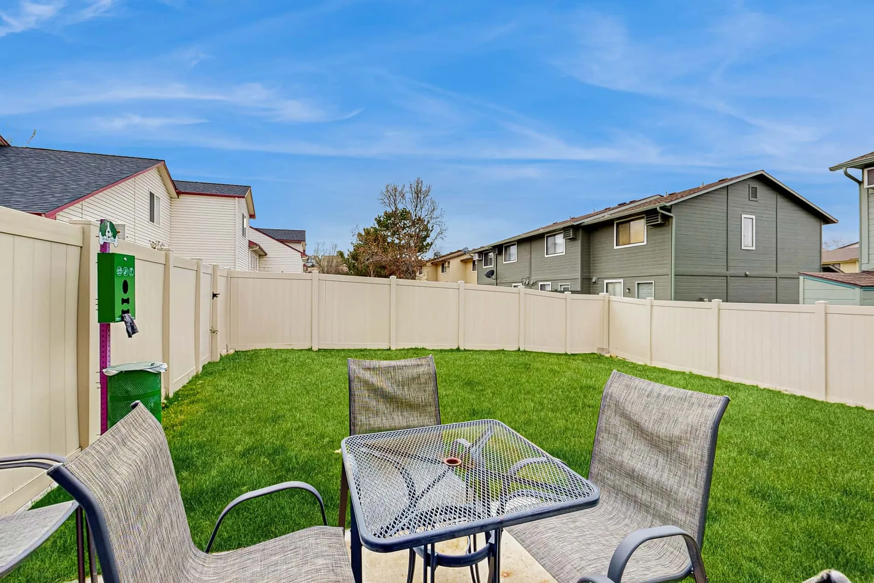 A fenced grassy outdoor seating area with a metal table and chairs.