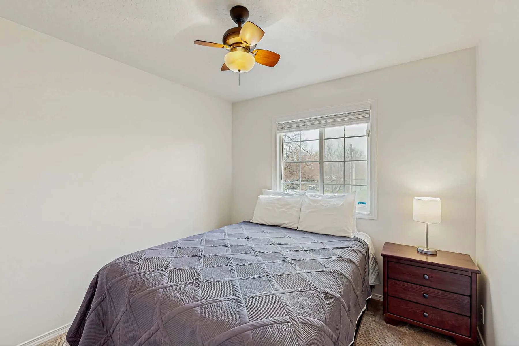 A bedroom with a neatly made bed, a window, and a bedside table.