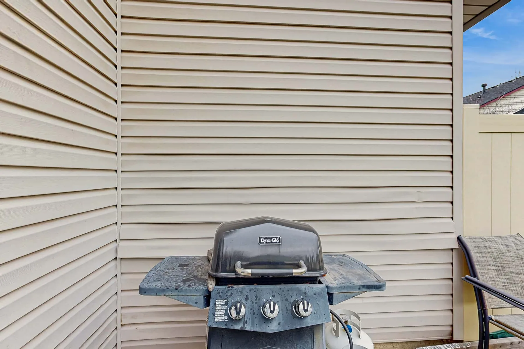 An outdoor grill sits beside the house against light-colored siding.