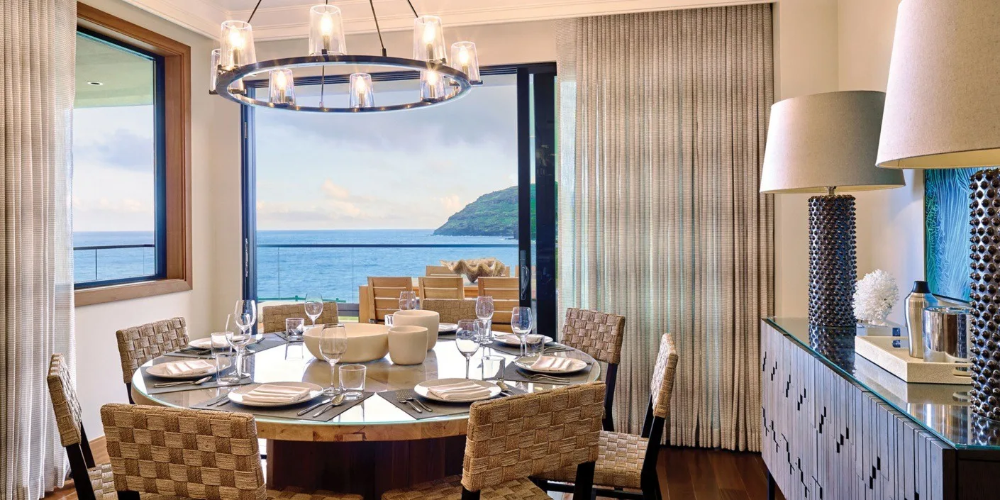 Comedor con una mesa redonda junto a grandes ventanales con vistas al agua.