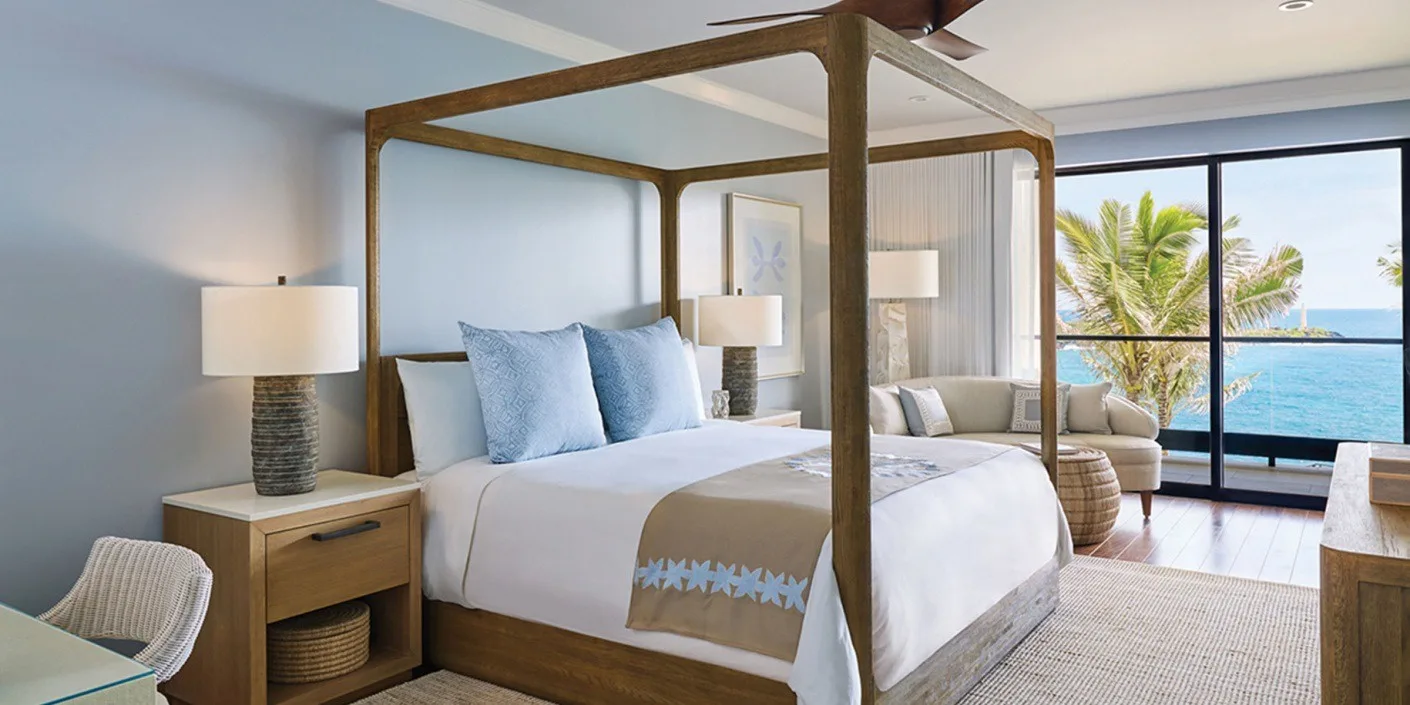 Un dormitorio con una cama con dosel junto a grandes ventanales con vistas al mar.