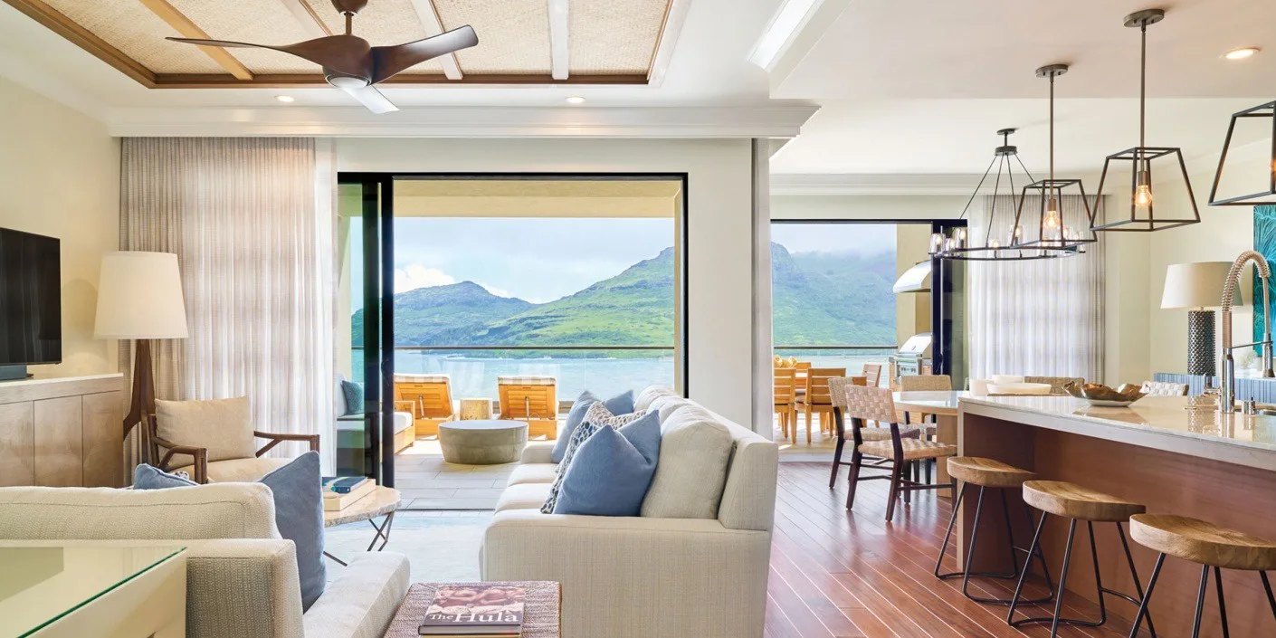 Una luminosa sala de estar y comedor da a un balcón con vistas al agua y las montañas.
