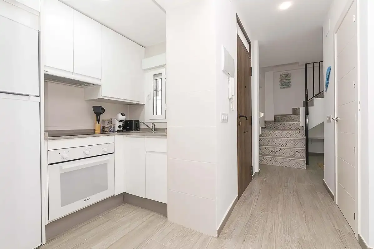 A bright kitchen opens onto a hallway with stairs at the far end.