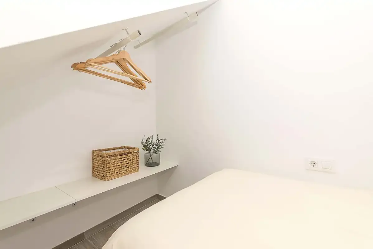 A bedroom with a bed, wall shelf, and clothes hangers.