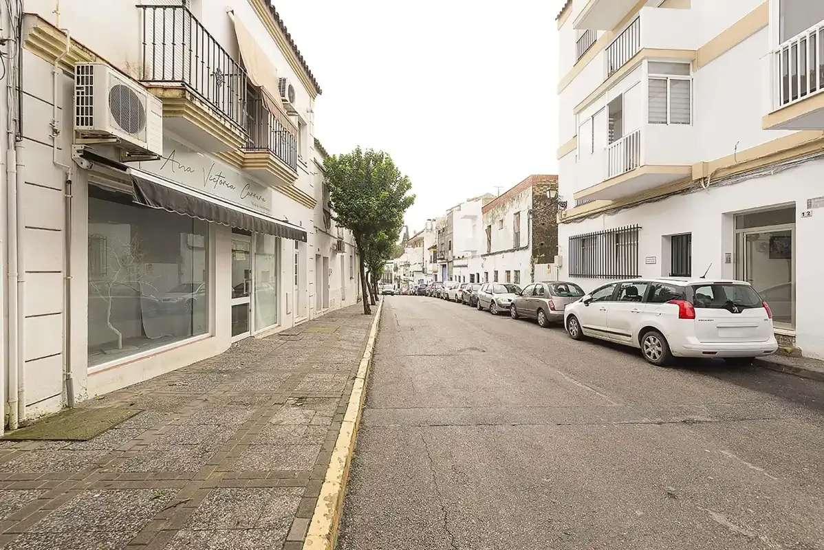 A quiet-looking street lined with white buildings and parked cars.